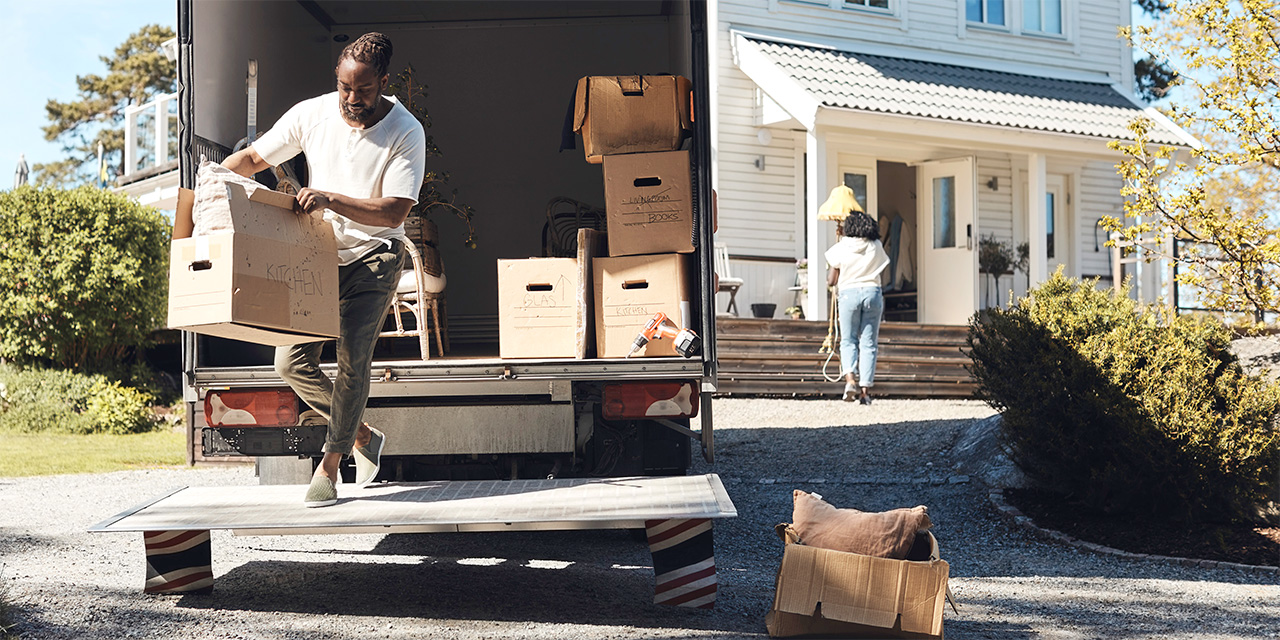 A man unloads boxes from a moving truck in front of a white house.
