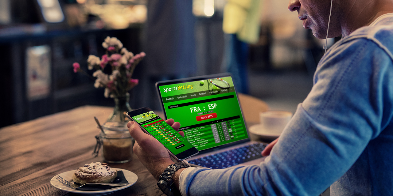 Man using online sports betting services on phone and laptop Man using online sports betting services on phone and laptop