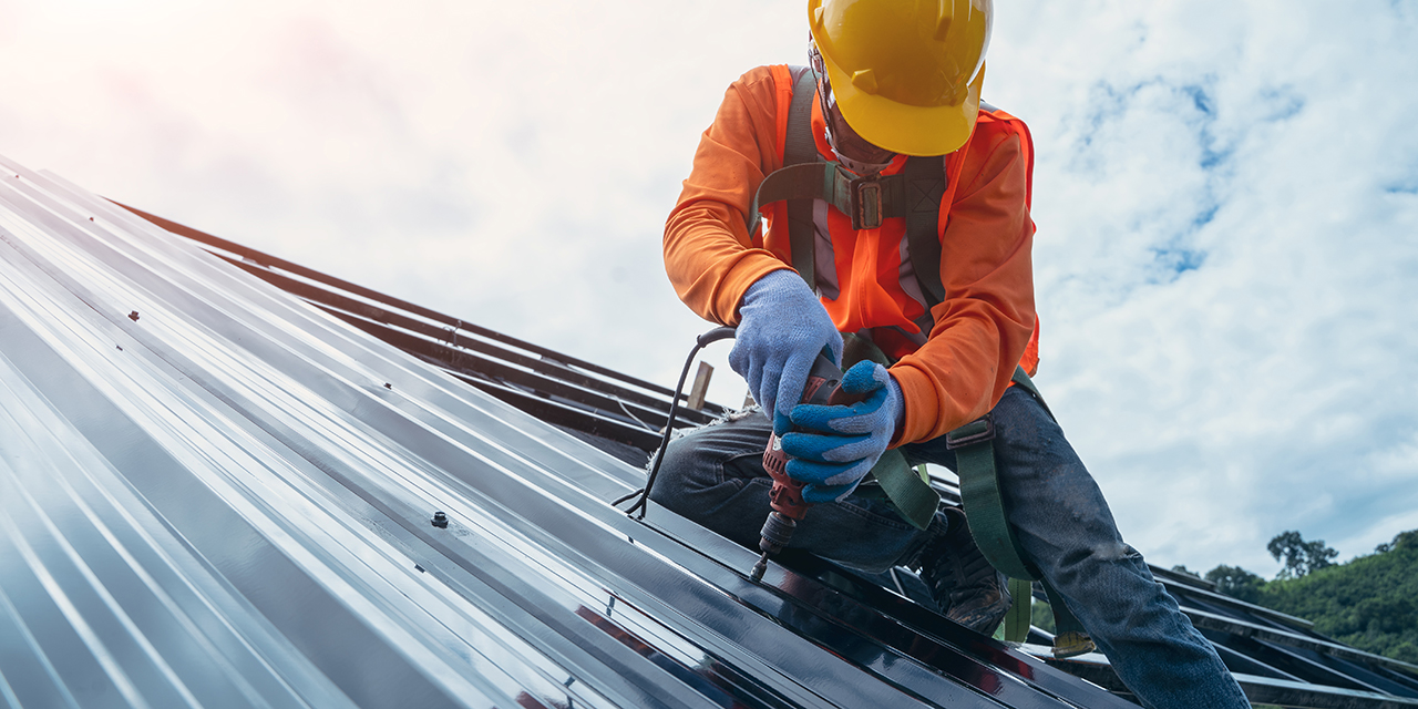 professional roofer in orange jacket and yellow hardhat installing metal roofing panels against a cloudy sky professional roofer in orange jacket and yellow hardhat installing metal roofing panels against a cloudy sky